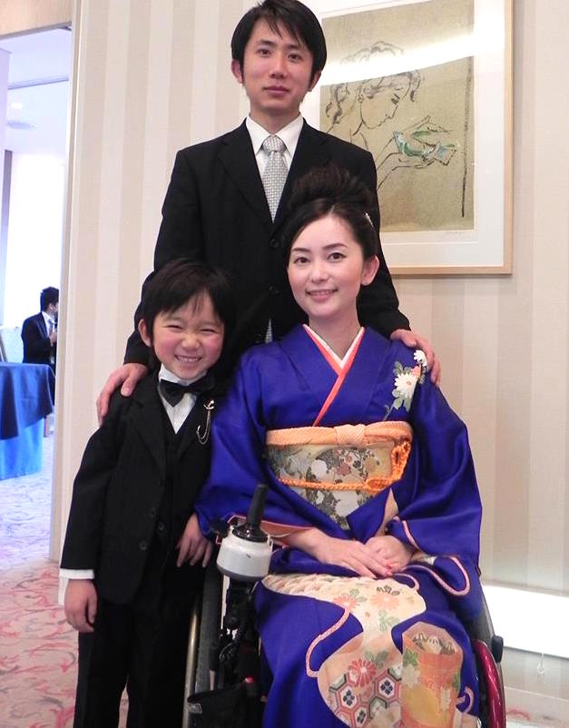 【写真】青紫色の着物を着て車椅子に乗って微笑んでいるゆりこさんとスーツを着て微笑んでいるよういちさん、笑顔のえいいちくん