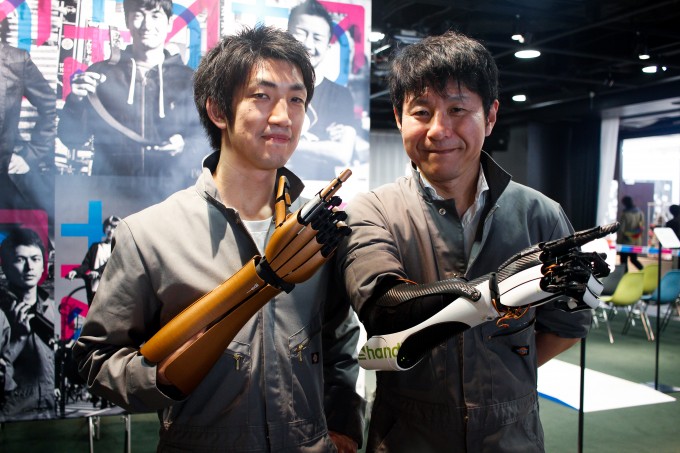 【写真】筋電義手のはんでぃーをつけてポーズを決める開発者のこんどうさんと義手ユーザーのもりかわさん