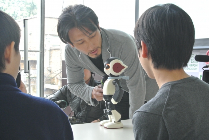 【写真】小型ロボットを操作するたかはしさん。子どもたちは真剣に興味深そうにロボットを見つめている。