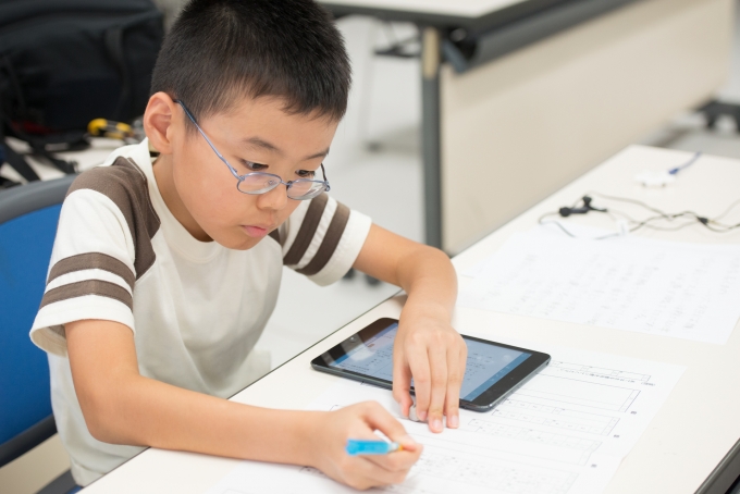 【写真】あいぱっどを机の横に置いて勉強をする子ども。とても真剣な表情をしている。