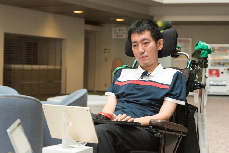 【写真】車椅子に座りアイパッドで作業をしているおんださとしさん