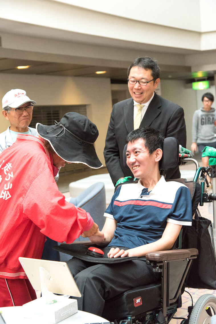 【写真】笑顔で握手をするおばあちゃんとおんださとしさん。おじいちゃんと秘書の坂田さんが見守っている