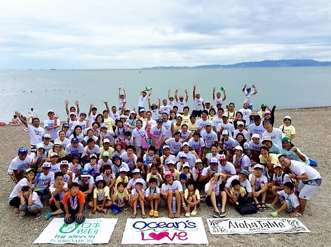 【写真】オーシャンズラブのメンバーが、砂浜で撮影した集合写真。元気よく手をあげて写るメンバーもいる