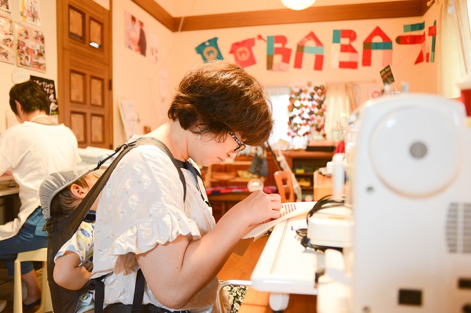 【写真】子どもを背負いながら裁縫をするメンバー