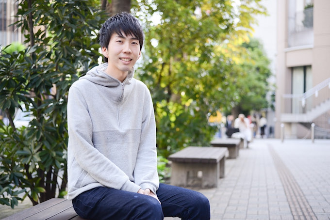 【写真】街頭のベンチに座り微笑んでいるまつおかそうしさん