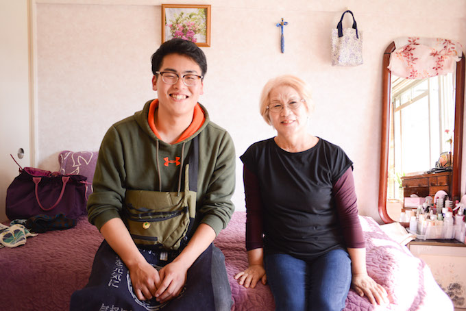 【写真】おきあきさんの部屋にあるソファに一緒に座り笑っているまつおかさんと利用者のおくあきさん。