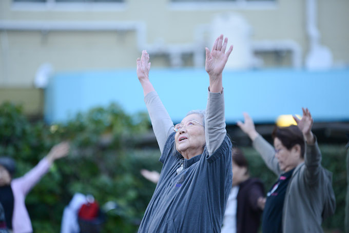 【写真】ちぃちゃん体操をしている参加者。手を空に伸ばす。表情ものびのびしている。