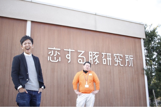 【写真】こいするぶたけんきゅうじょの前で笑顔を見せる、スタッフのありたさんとにしやまさん