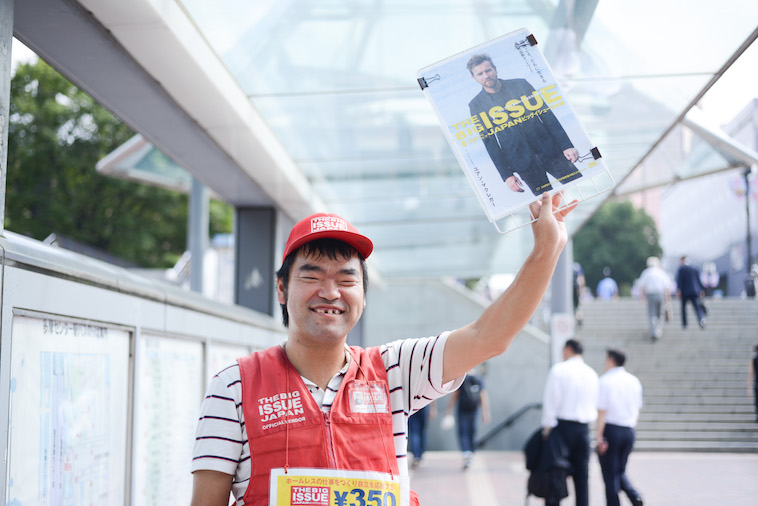 【写真】路上でビッグイシューの雑誌を高々と掲げているホームレスの方