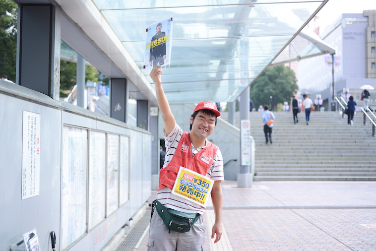 【写真】ビッグイシューを笑顔で堂々と掲げるやましたさん