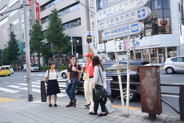 【写真】路上で高くビッグイシューを掲げる山崎さんとライターのにしやまたけしさん、くどうみずほ