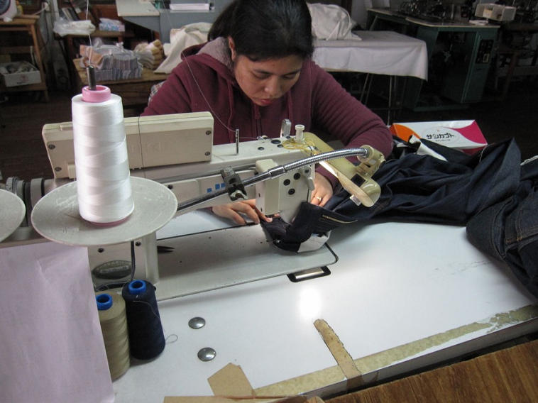 【写真】ミシンをを使い、真剣な眼差しでジーンズを縫う女性。