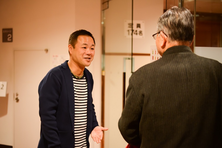 【写真】お客さんと話すあおやまさん。ささやかに笑みを浮かべている。