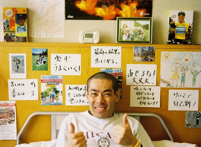 【写真】たくさんのメッセージと写真の前で微笑む、おおくぼじゅんいちさん