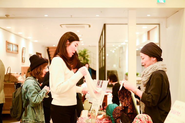 【写真】参加者にプロダクトの説明をするつのださん。参加者は、プロダクトを手にとっている