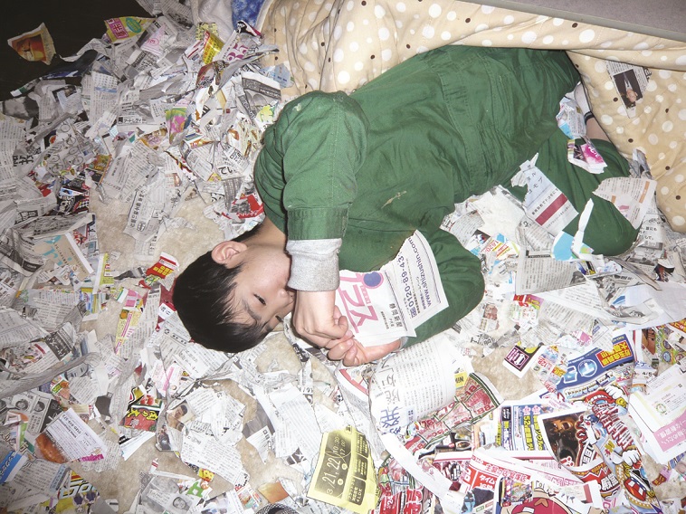 【写真】みどりさんの息子たけしくんが広告チラシや新聞紙の上に寝転がり、夢中でそれらをちぎっている。