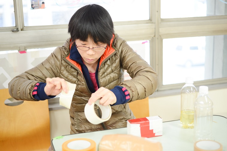 【写真】ガムテープを使い作品を作る利用者のたかはしまいさん。集中している。