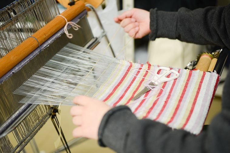 【写真】赤、白、グレー、黄色の糸を組み合わせて図柄を表現する利用者。繊細な手作業を行なっている。