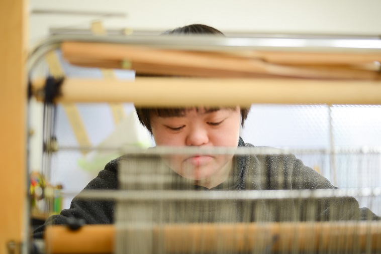 【写真】はたおり機の前に座り、真剣に作業している利用者。