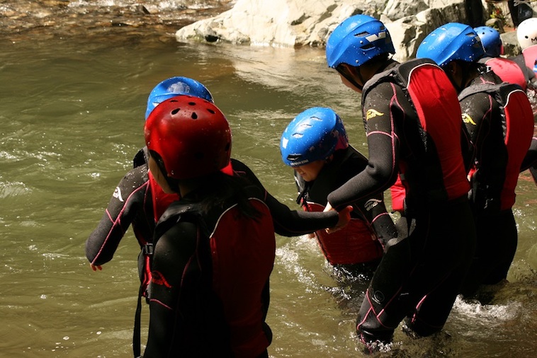 【写真】救命胴衣とヘルメットをつけて、川に足を踏み入れる子どもたち。少しの不安とワクワクした空気を感じる。