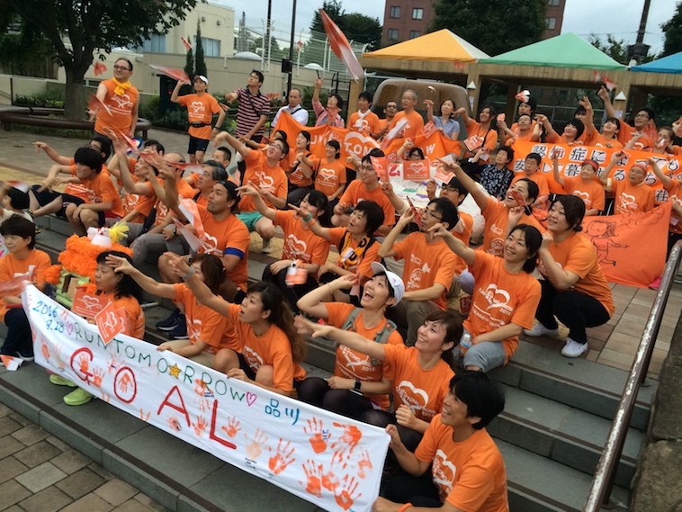 【写真】揃いのTシャツをきて、集まっている大勢の人々。全員で紙飛行機を飛ばし、楽しい空気が漂っている。