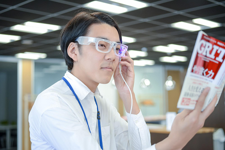 【写真】透明なフレームのオトングラスをつけて本を読んでいるしまかげけいすけさん