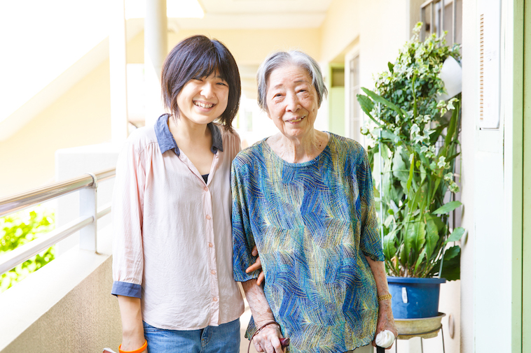 【写真】利用者の高齢女性に腕を絡めて微笑む、たかすさん