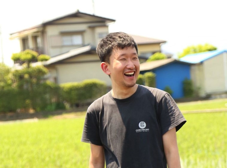 【写真】笑顔で田んぼの前に立つおおたなおきさん。