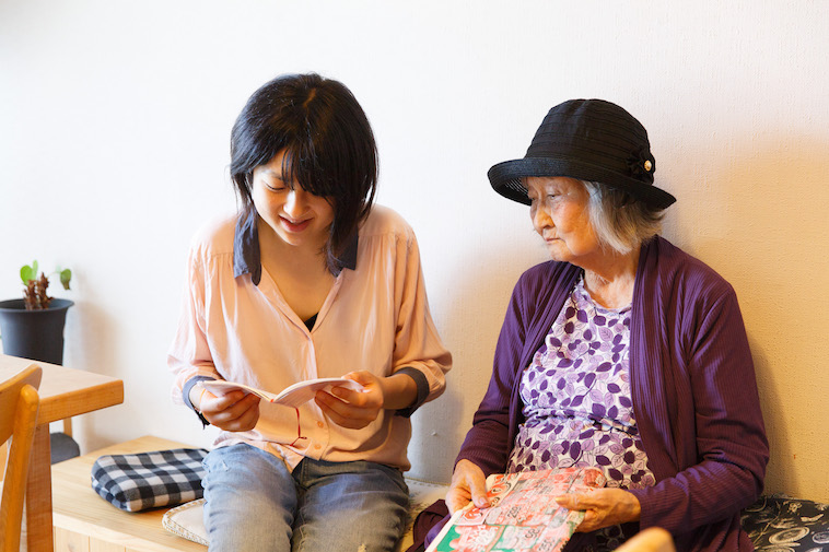 【写真】おばあさんの隣に座り、小さなノートを開いて覗き込むたかすさん