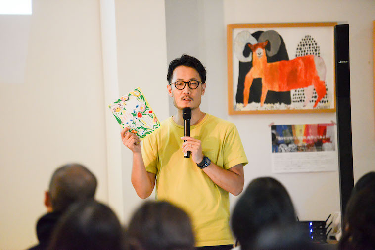 【写真】子どもの村が発行した冊子を片手に参加者の前で語る、たきたさん