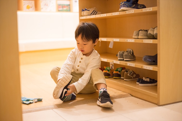 【写真】玄関に座り少しずつ自分で靴を履こうとする子ども