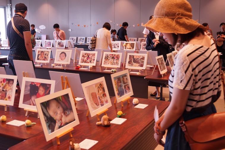 【写真】机に並べられた子どもたちの写真を見入る来場者の女性