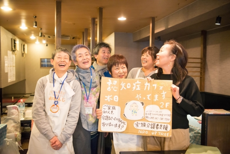 【写真】看板を持って眩しい笑顔で話すスタッフの皆さん