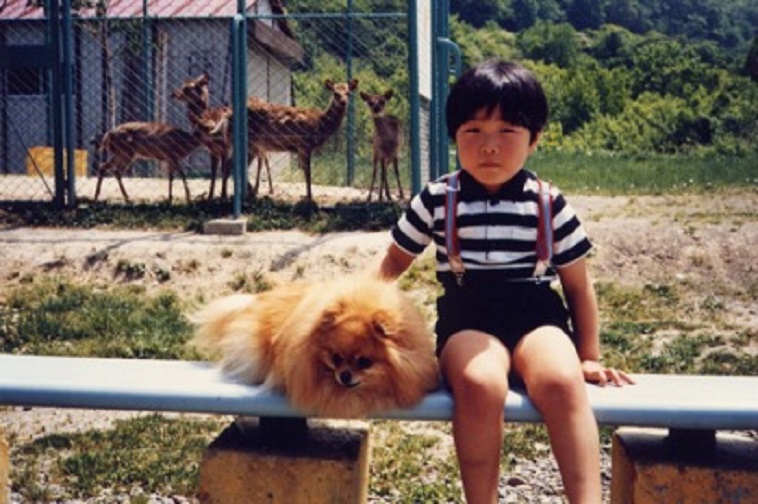 【写真】こばやしりょうこさんの息子さんの幼少期の頃の写真。犬と一緒に写っており、後ろには子鹿が3頭いる。