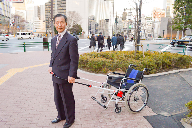 【写真】歩道でJINRIKIを取り付けた車椅子を持つ株式会社JINRIKIのなかむら社長