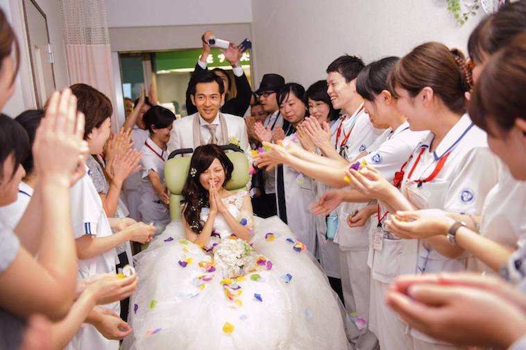 【写真】病院のスタッフに拍手をされながら迎えられるウェディング姿の新郎と車椅子の花嫁