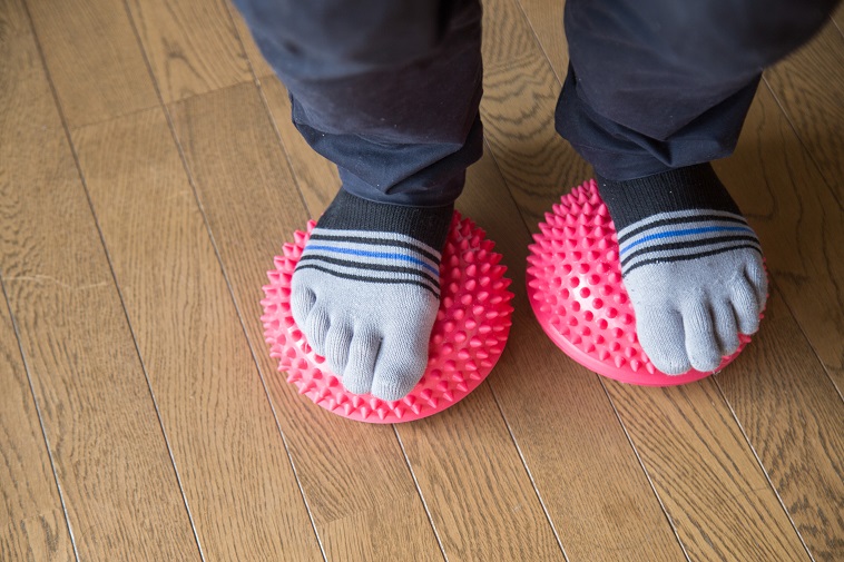【写真】いぼがついたリハビリ用の道具の上に立つちばさん