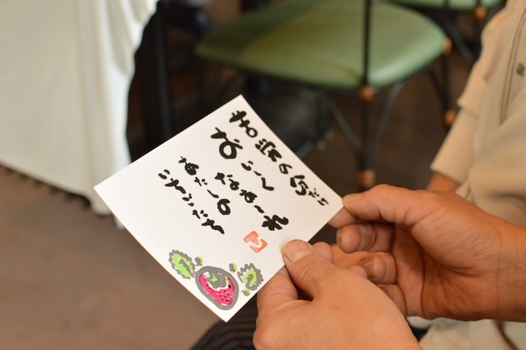 【写真】しみずさんの書のアップ。書には「苦労の分だけおいしくなあれ。わたしのいちごたち」という言葉と、いちごのイラストが描かれている。