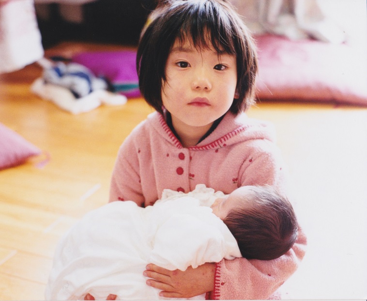 【写真】幼少期のきどかなえさん。赤ちゃんを抱っこしている。
