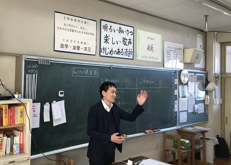 【写真】出張授業をしているたにやまさん。黒板の前で身振り手振りを交えて楽しそうな様子で説明している。