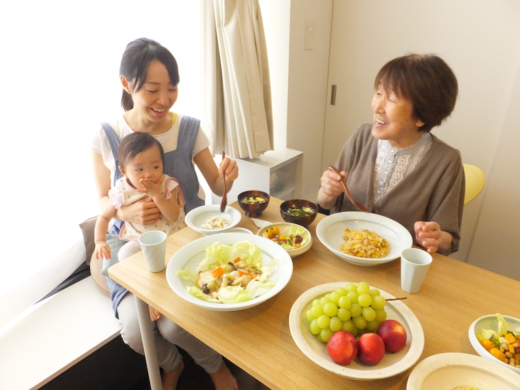 【写真】てまるのお皿、スプーンを使って食事をする笑顔の高齢者と赤ちゃんを抱く女性