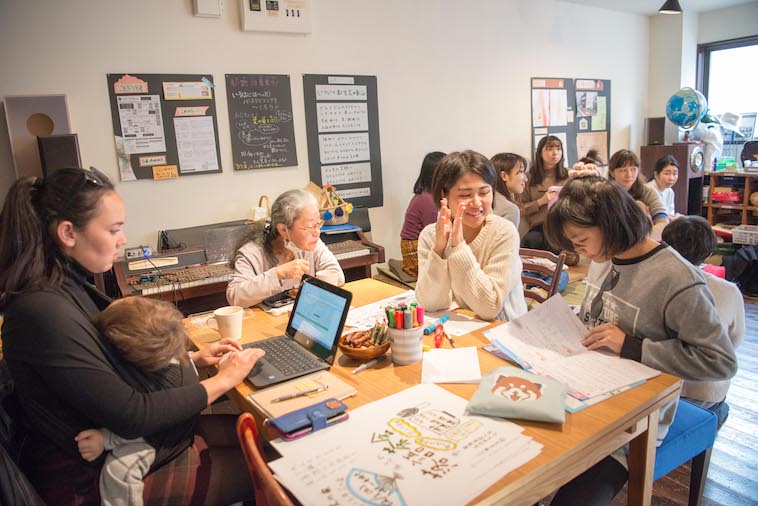 【写真】パソコンで仕事をする人、その近くでは雑談をしているお母さんたちや、一人でくつろぐおばあちゃんが
