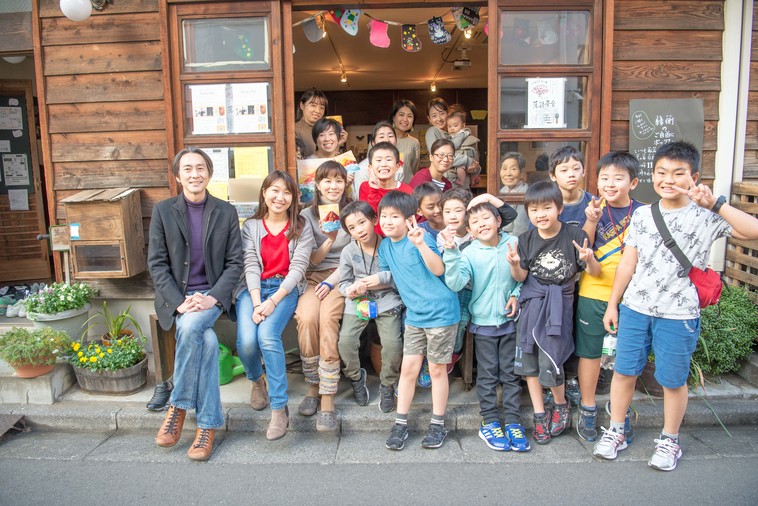 【写真】縁側にたくさんの子どもや大人が混ざって並び、カメラに向かって笑顔を向けている