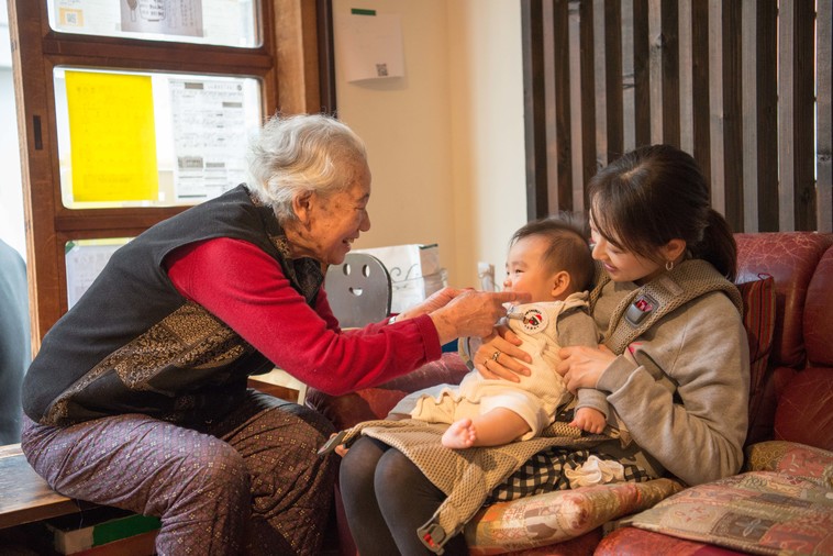 【写真】おばあちゃんがお母さんの膝に座っている赤ちゃんのほっぺを笑顔でつついている