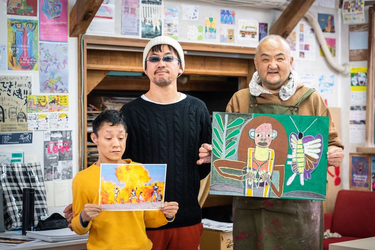 【写真】スウィング代表の木ノ戸さんと、自分の作品を持って並ぶメンバー2人