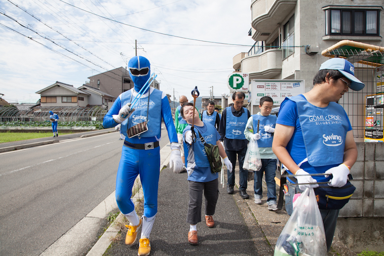 【写真】道路で清掃活動の「ゴミコロリ」を行なっている様子。青いTシャツや、青い戦隊レンジャーの衣装を着ている
