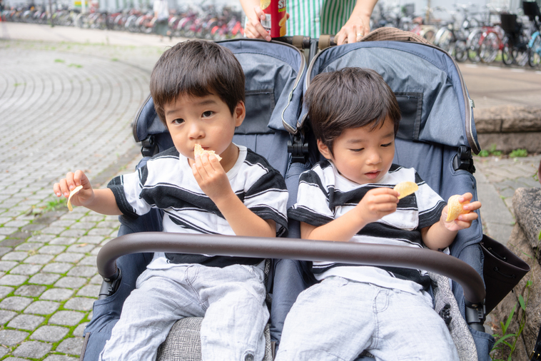 【写真】双子用ベビーカーにのって、お菓子をたべているいながきさんの二人の子供たち