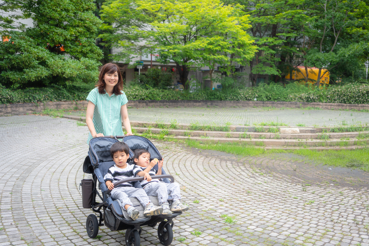 【写真】公園で、双子用のベビーカーに子供をのせ、笑顔で歩いているいながきさん。