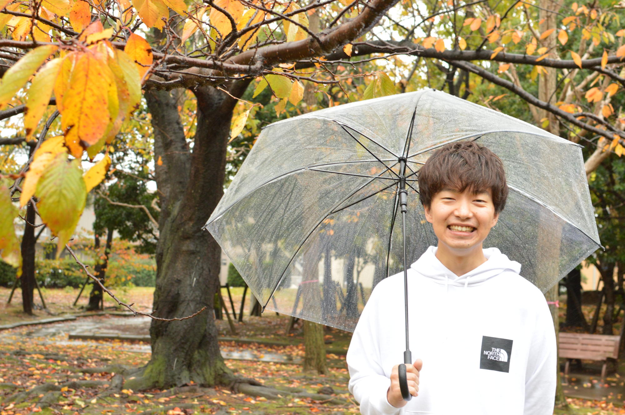 【写真】雨が降っている中、傘をさして笑顔のかわさきすぐるさん