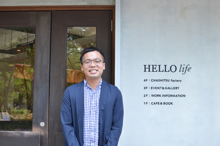 【写真】ハローライフの事務所の前で笑顔で立っているしおやまりょうさん